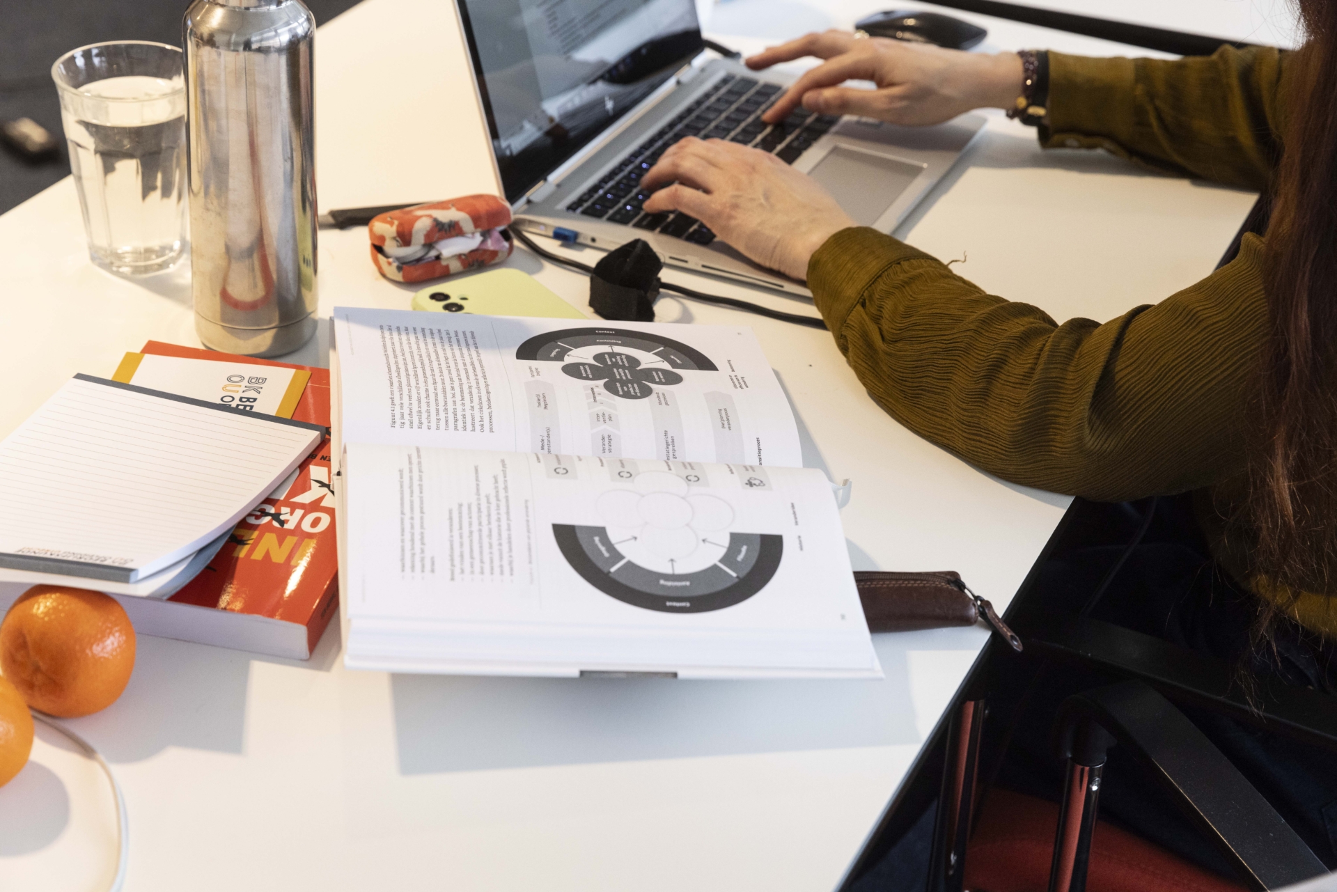 Student post-hbo Bedrijfskunde doet onderzoek met laptop en studieboek.